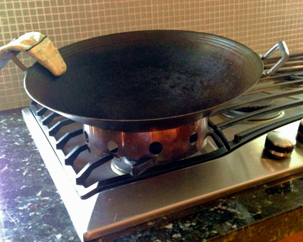 Lightweight, thin walled, round bottom cast iron wok sits on wok ring on top of Viking gas stove with horizontal iron grate. 